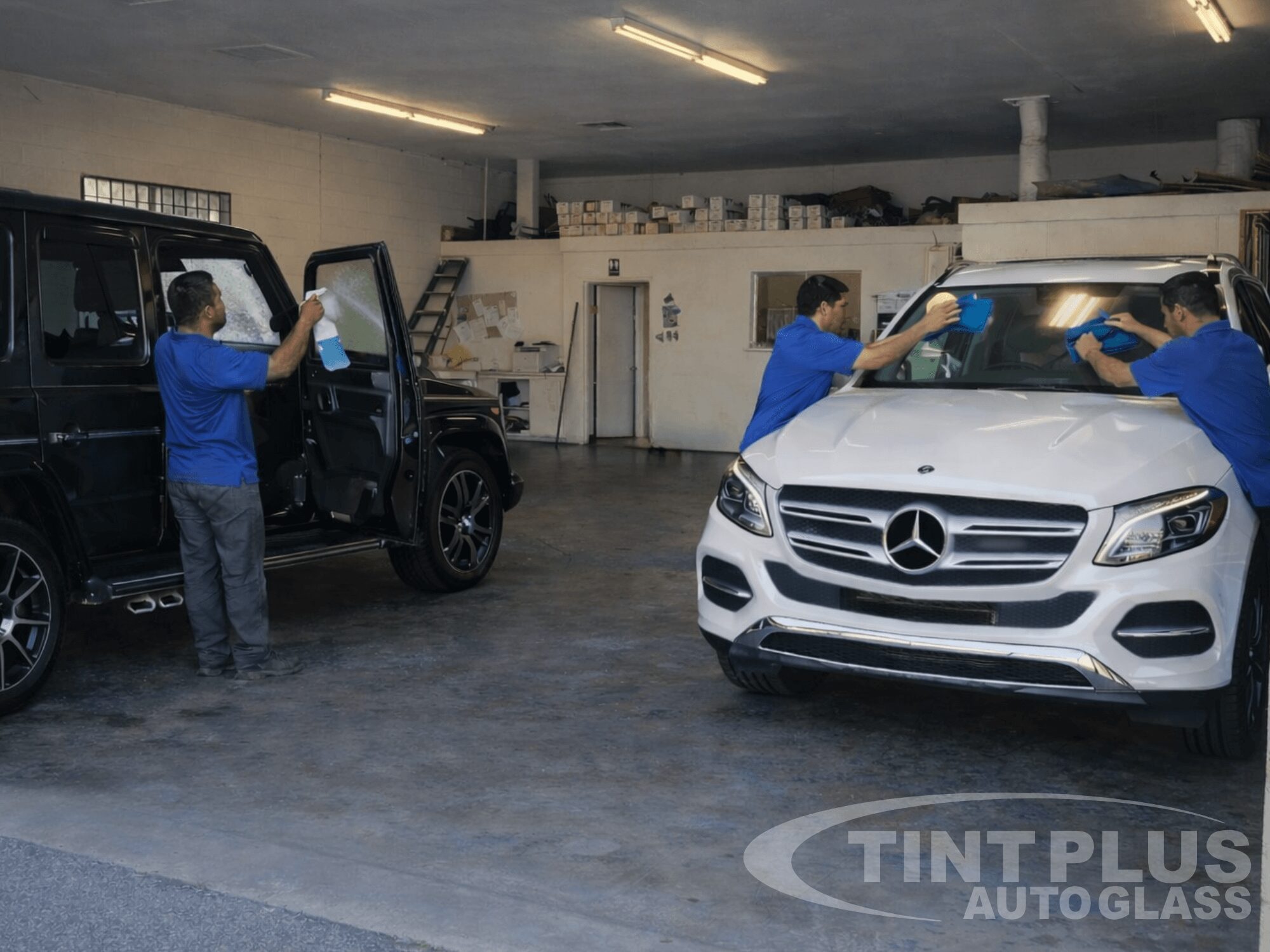 Technicians at Tint Plus Auto Glass in Hanford CA installing and cleaning window tint on a Mercedes SUV inside a professional auto glass workshop.